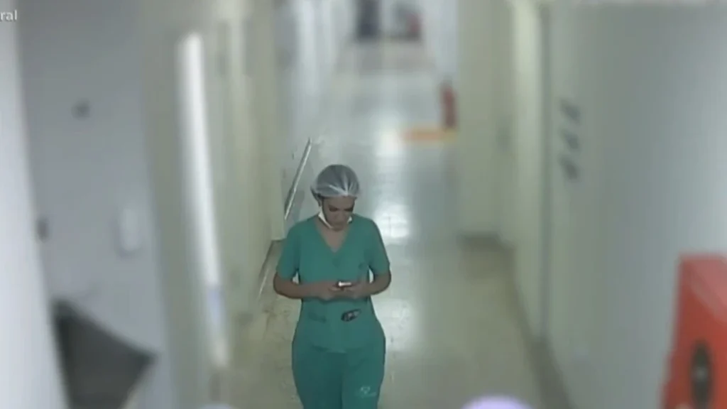 Cena de hospital com mulher de jaleco segurando celular, com olhar desconfiado.